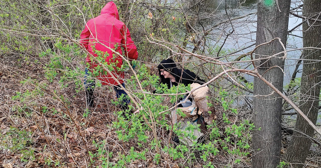 Two people cleaning up trash by the river